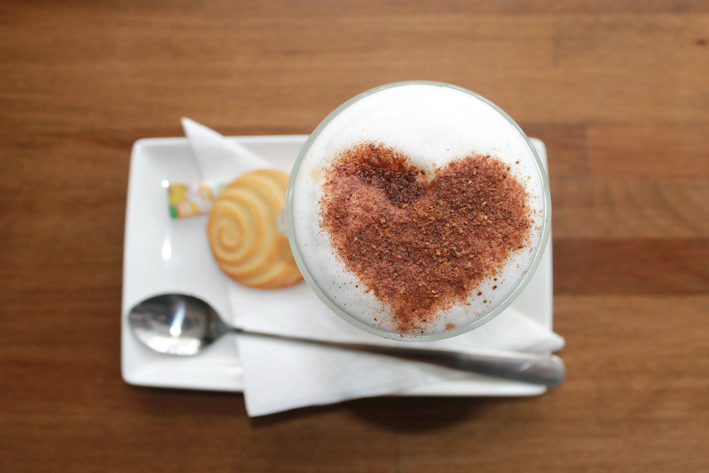 A latte with cocoa on top sprinkled into the shape of a heart. 