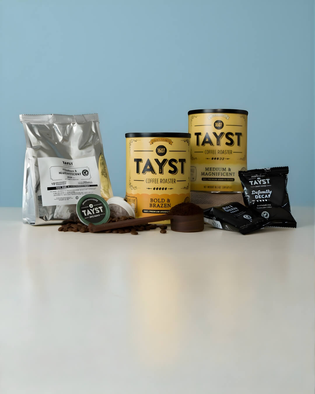 Tayst coffee products including bags, tins, and a pod on a light blue background