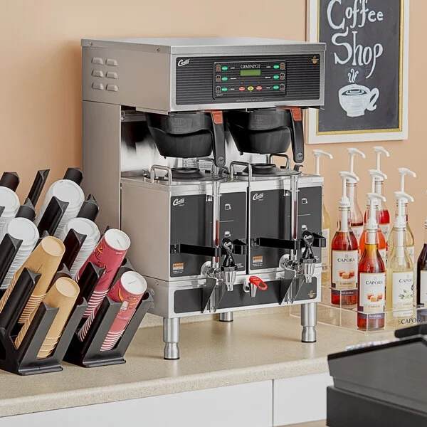 Coffee machine on a counter with various coffee cups and bottles in a coffee shop setting.