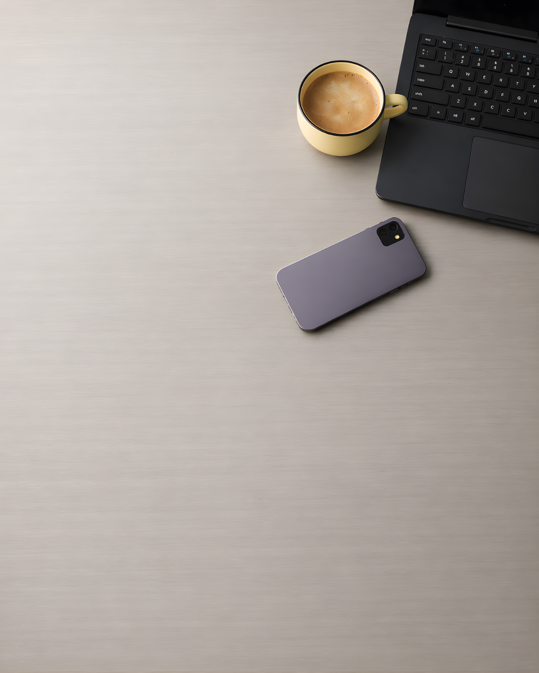 Phone, coffee cup, and laptop on a light gray surface