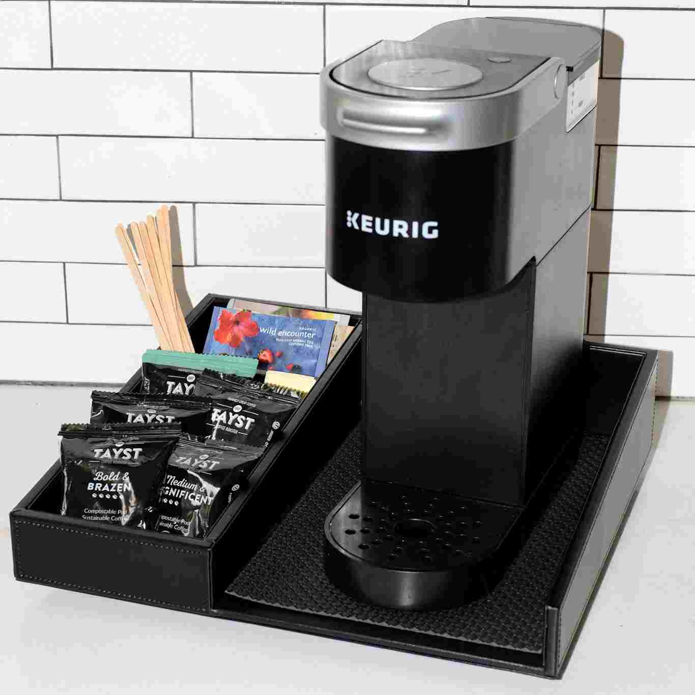 Black Keurig coffee machine with a tray of coffee pods on a tiled kitchen counter.