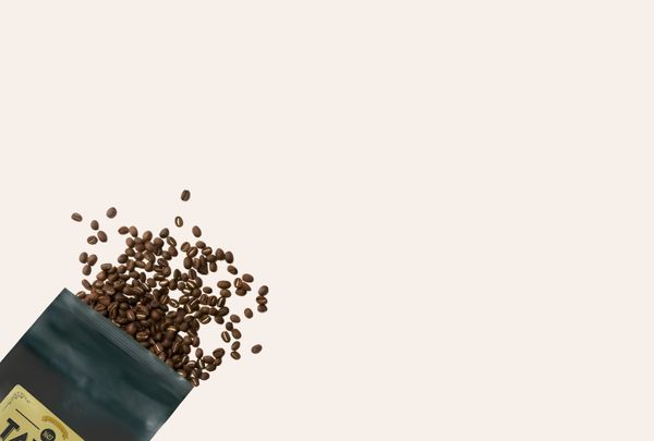 Open bag of coffee beans spilling out on a beige background