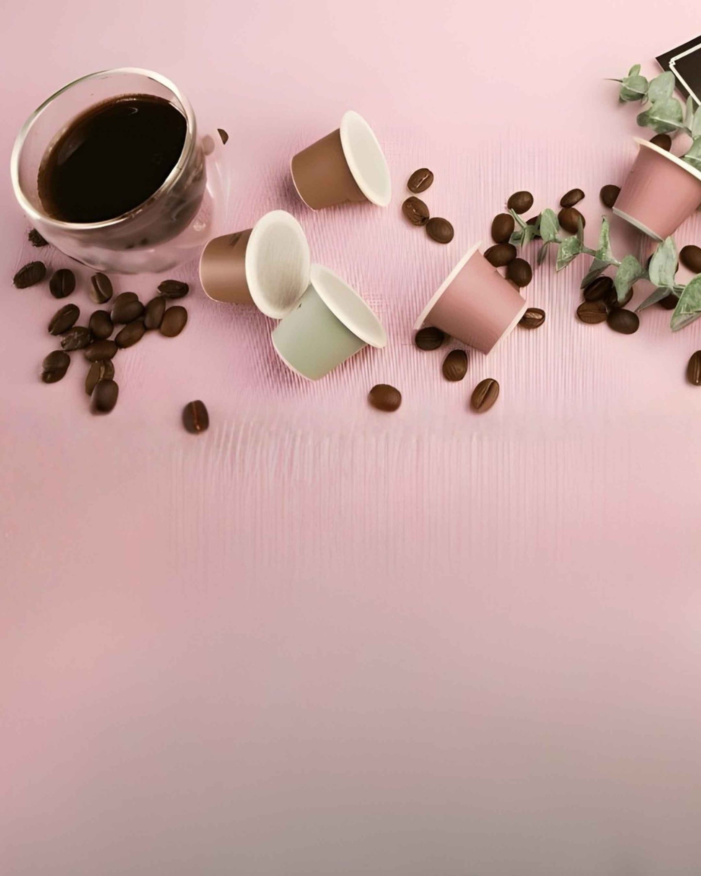 Coffee cup, tayst nespresso capsules, and coffee beans on a pink surface