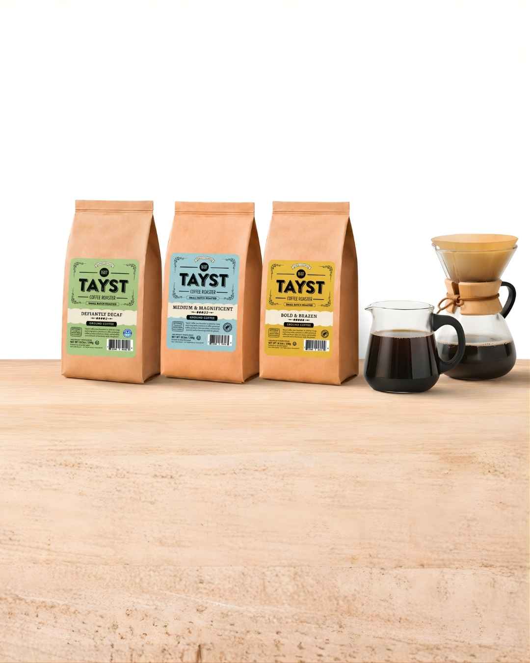 Tayst coffee bags including decaf, medium roast, and bold roast next to a pour-over coffee brewer and glass carafe