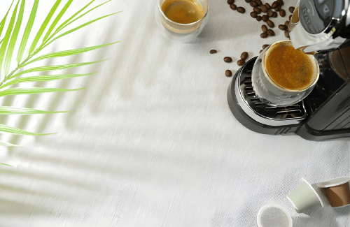 Coffee-making process with a coffee machine, cup, and coffee beans on a white surface.