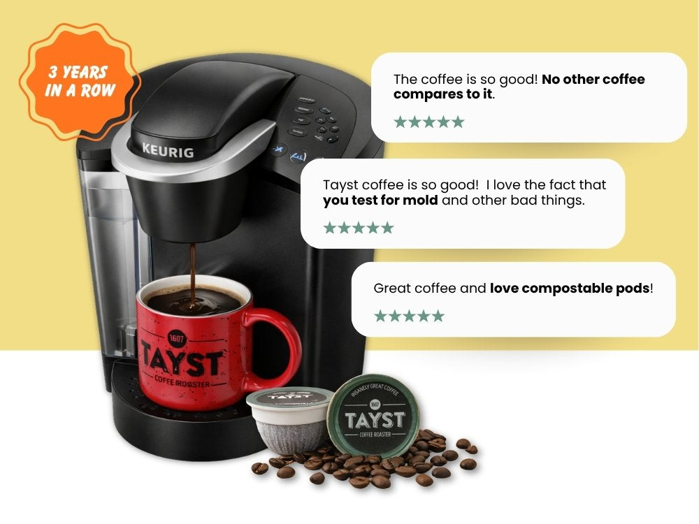 Keurig coffee maker with a red mug, Tayst coffee beans, and compostable pods on a yellow background.