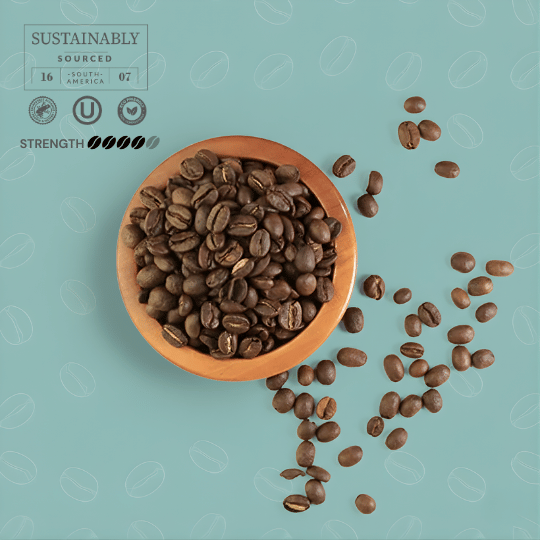 Wooden bowl filled with coffee beans on a light blue background with scattered beans.