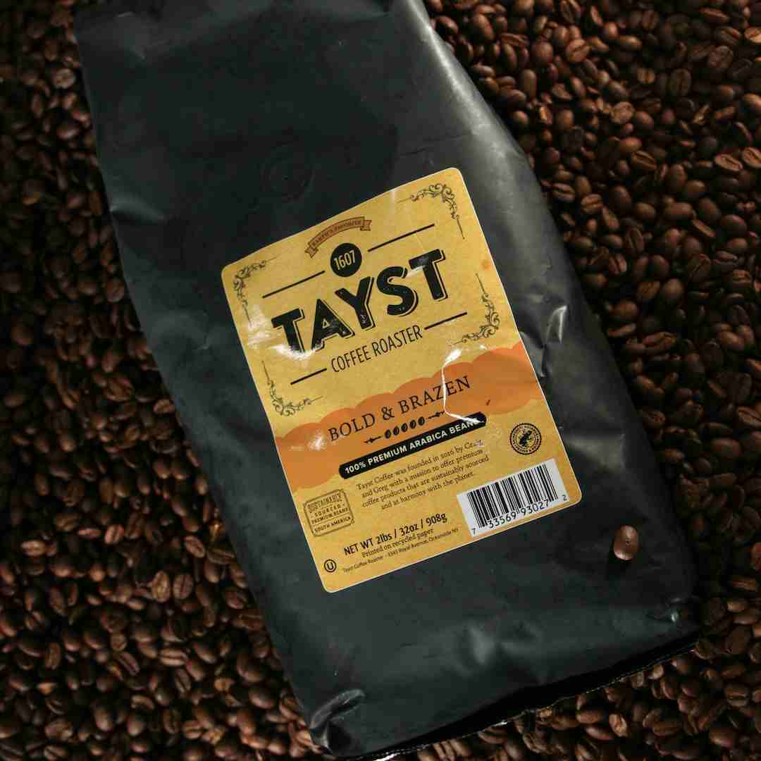 Coffee bag with 'TAYST' label on a bed of coffee beans