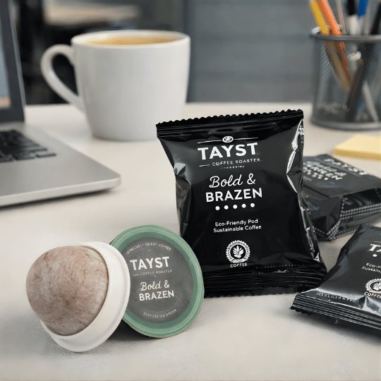 Tayst coffee singles on a desk with a laptop in the background